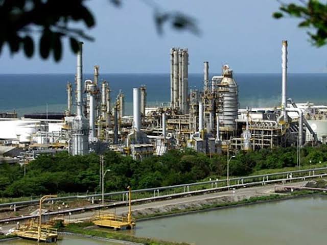 Complejo de refinería industrial junto al mar, rodeado de vegetación.